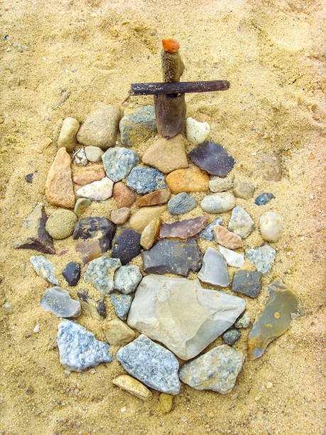istock Small grave with cross in beach sand made of pebbles. 1973315990
