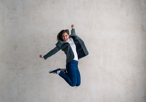 Freedom, success and jump, young woman with energy and motivation in celebration of winner deal. Ecstatic female with in-ear headphones, jump for joy.