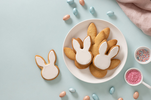 Easter homemade bunnies glazed shaped cookies and eggs on blue background. View from above. Festive food and snacks. Greeting card with space for text.