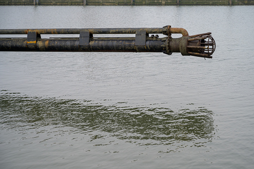 Side view of a dredge drag head of a suction dredge barge above water in a harbor. Used to remove sediment inside in order for ships to be able to pass through at low tide.