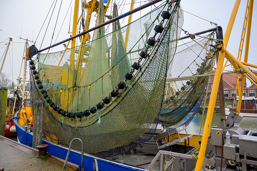 Drag net on a colorful crab or shrimp fishing boat in the historic harbor of Neuharlingersiel with part of the on board processing equipment visible as the shrimp is cooked at sea to keep fresh