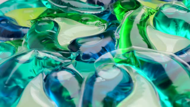 Washing gel capsule pod with laundry detergent, rotation in circle. Full frame shot of blue-green liquid laundry detergent pods, Turning.