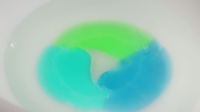 Washing gel capsule pod with laundry detergent dissolves in hot water. Full frame shots of blue-green liquid laundry detergent pods
