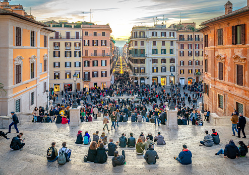 Rome, Italy - December 2 2018: Sunset on the crowded Spanish Steps that lead to Piazza di Spagna with Via dei Condotti in the background.