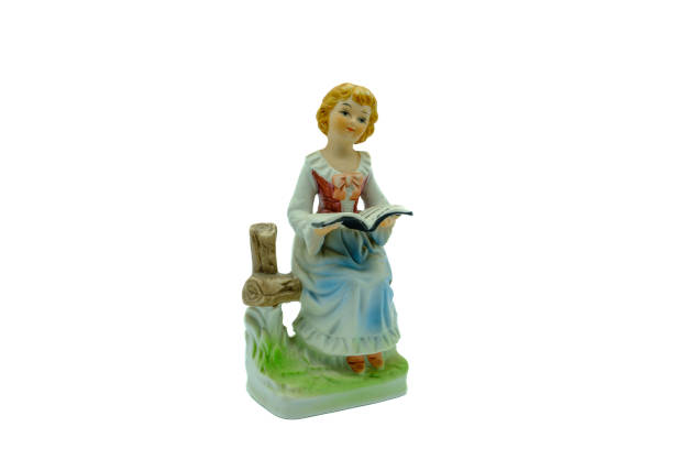 porzellanfigur eines jungen mädchens, das sitzt und aus einem buch liest - ceramic figure stock-fotos und bilder