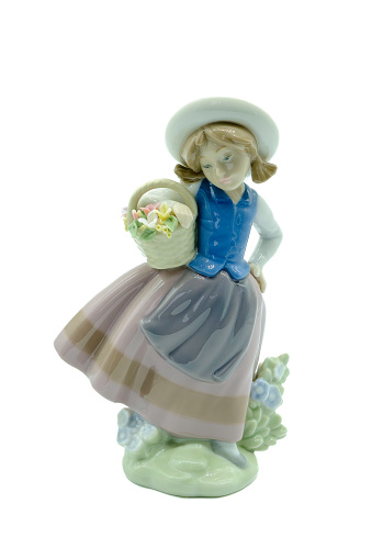 Antique Small porcelain figure of a girl in a bonnet blue brown and white clothing carrying a vase of yellow pink and white flowers.