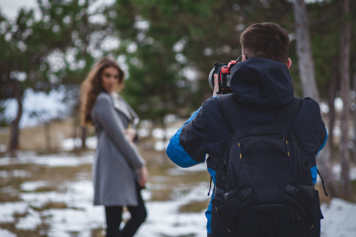 Young photographer man taking photos about a beautiful woman in nature in winter time