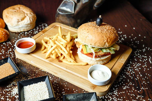 A close-up view of a hamburger and French fries placed on a wooden cutting board.