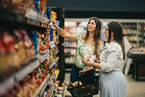 Two female friends choosing at a product on rack to buy in supermarket