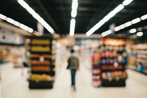 Defocused view of a woman walking in an aisle in a large supermarket while doing some grocery shopping