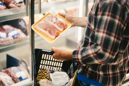 Close-up of a man looking at a package of steaks in an supermarket aisle while doing his grocery shopping
