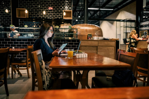 istock Young woman holding digital tablet and using laptop at restaurant 1973413472