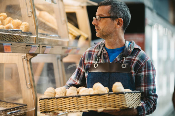 Clerk carrying a basket of freshly-baked bread to place in a display in supermarket aisle
