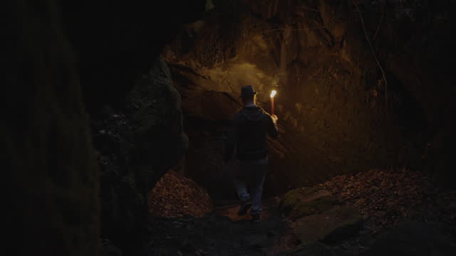 Man Holding A Burning Torchlight Exploring Forest Cave Landscape In Dark Night