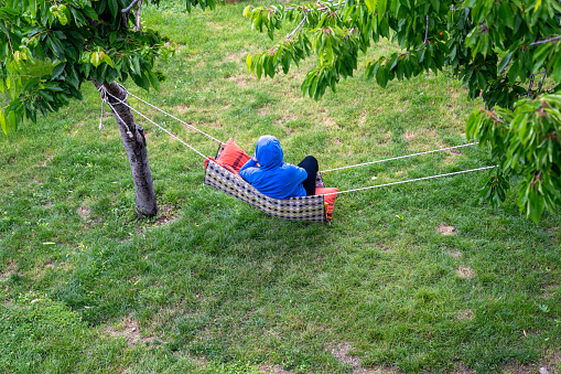 high angle photo of woman wearing a blue hoodie sweater sitting on home made hammock in garden. Shot with a full frame mirrorless camera in outdoor.