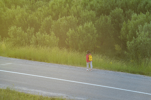 High angle photo of woman wearing red coat walking on single lane country road. Shot under daylight.