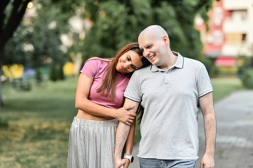 Female Trying To Lift The Mood Of Cancer Patient Husband While Walking Outside Holding Hands