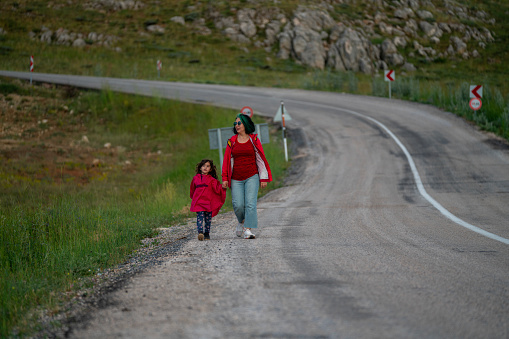 Photo of mother and 5 years old daughter walking by single lane country road. Shot during springtime under daylight.