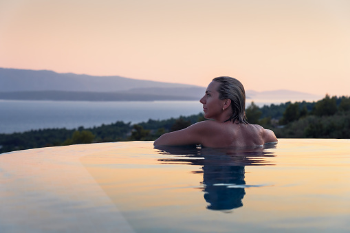 Beautiful young woman relaxing in infinity swimming pool at sunrise or sunset