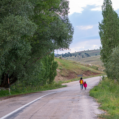 Photo of mother and 5 years old daughter walking by single lane country road. Shot during springtime under daylight.