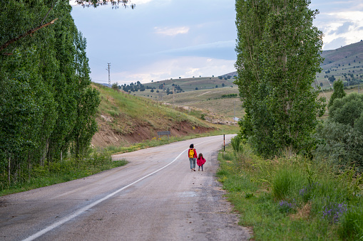 Photo of mother and 5 years old daughter walking by single lane country road. Shot during springtime under daylight.