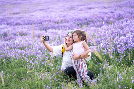 Candid photo of mature mother and 5 years old daughter taking selfie photo in purple lavender field. Shot under natural light with a full frame mirrorless camera.