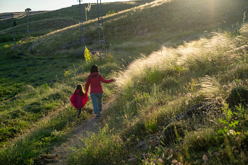 Photo of mother and 5 years old daughter walking by single lane country road. Shot during springtime under daylight.