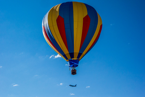 A hot air balloon flies in the sky above Colorado as an airplane in the background flies beneath it..