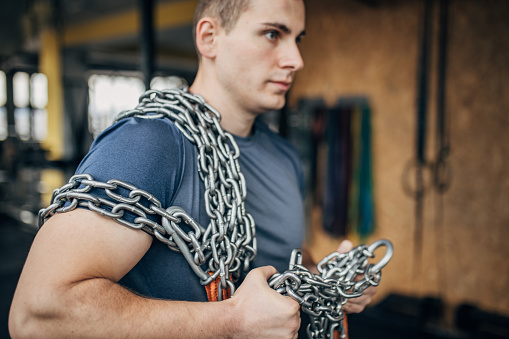 One man, fit male carrying chains in gym.