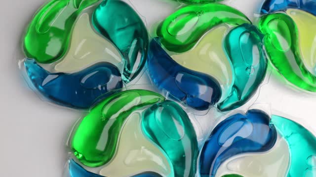 Washing gel capsule pod with laundry detergent, rotation in circle. Full frame shot of blue-green liquid laundry detergent pods, Turning.