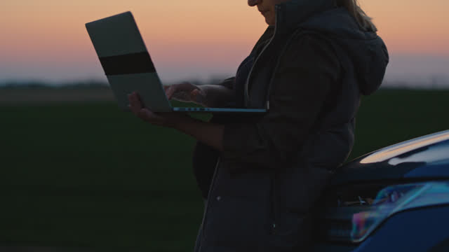 SLO MO Expectant Woman Using Laptop while Standing by Car in Farm during Blue Hour