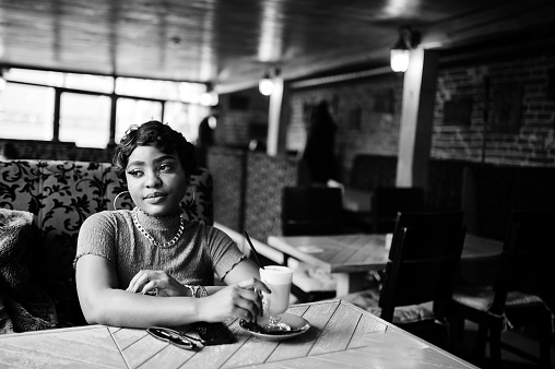 Urban young african american woman in pink top sit in cafe and drink latte coffee.