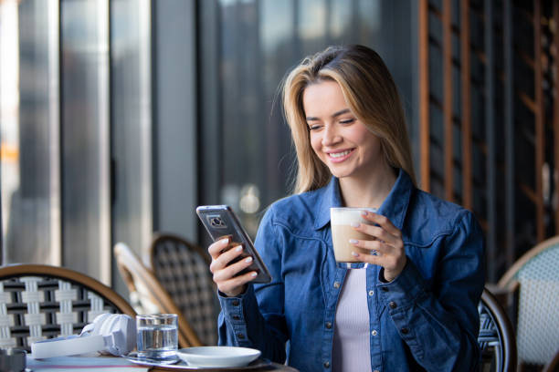 istock Sip and Scroll: Blonde Woman Enjoys Coffee While Engaging with Phone 1973620004