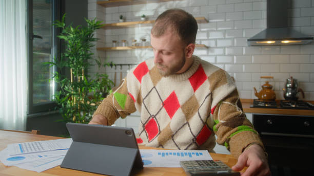 istock Adult man sit in the kitchen with tablet computer pay bills, use calculator count expenses, make budget control, manage finances, review overdue loan payments 1973651132