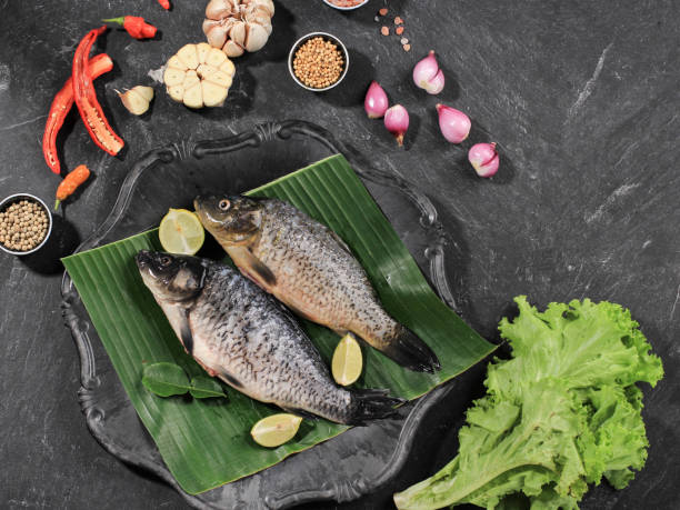 istock Raw Ingredients of Pesmol Ikan Mas (Gold Fish with Yellow Curry Spices). Pesmol Typically Fish Recipe from West Java, Indonesia. Can Made with Tilapia Fish (Ikan Nila) Too. On Black Background with Lemongrass, Garlic, Shallots, Lime Leaf 1973676930