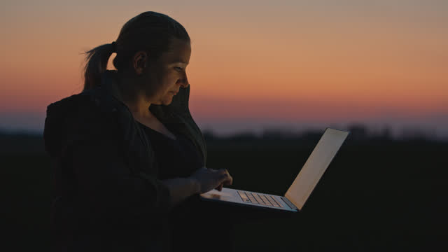 SLO MO Female Environmentalist Working on Laptop during Sunset. Female Farmer Holding Laptop in Farm Field.