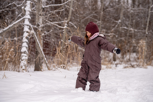 A sweet little girl is seen walking in the woods as she as she enjoys the cool fresh air and the crunch of fresh snow beneath her feet.  She is dressed warmly in a snowsuit, boots, hat and mittens as she expresses her joy with the season.