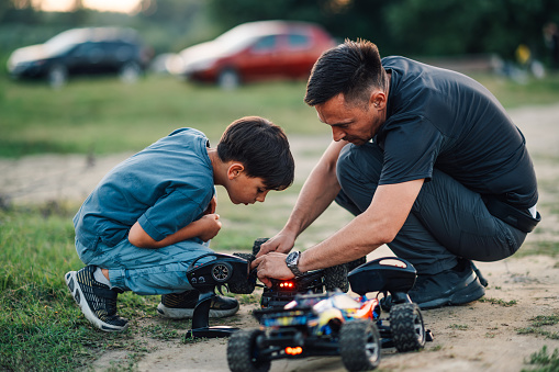 Middle aged father showing the issue with a wheel on his son's truck toy. They were playing with remote controlled toy cars and the boy's car overturned. The boy is carefully watching.