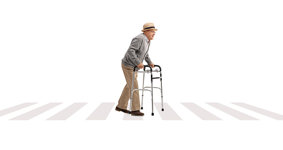 Full length profile shot of a senior man crossing a street with a walker isolated on white background