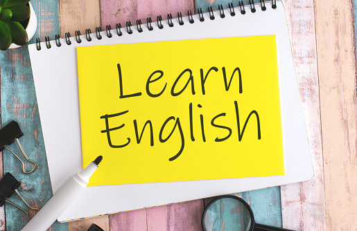 Text 'Learn English' written on a yellow sheet of paper with a black marker, placed on a multicolored wooden background, captured from a top view. concept of teaching international communication