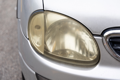 Hazy opaque yellowed front head lamp of car reduces light pass-through and driving visibility on the road