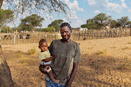 village , african family father and kid at the farm, kraal with goats in the background, Kalahari small livestock
