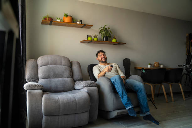 istock Man in living room with remote control, smiling 1973941047