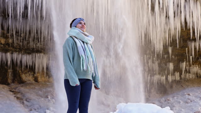 SLO MO Smiling Young Woman in Warm Clothes Standing near Peričnik Falls with Icicles Covered Rock in Triglav National Park, Mojstrana