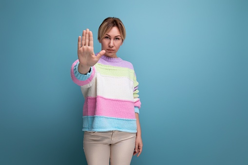 serious charming blond young woman showing stop sign with hand on blue background.