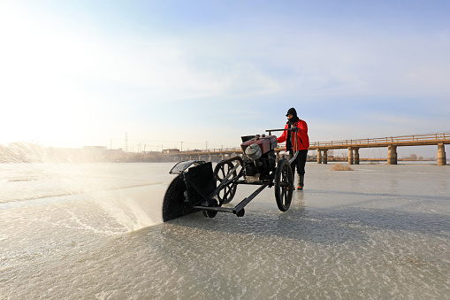 LUANNAN COUNTY, Hebei Province, China - January 22, 2021: Farmers use electric saws to cut river ice in the wild.