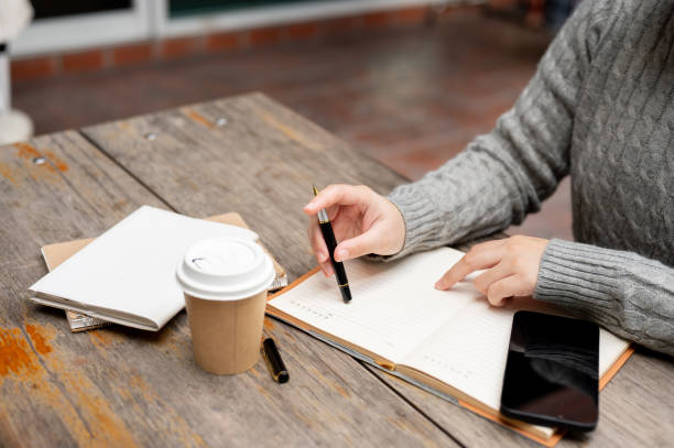 istock A close-up image of a woman working at a table outdoors, writing or taking notes in a notebook. 1974001037