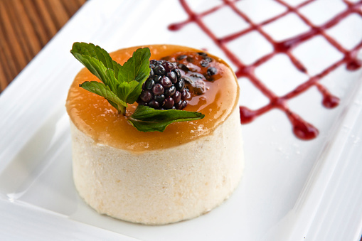 Cheesecake topped with guava and blackberry and strawberry jam, served on a white rectangular plate on wooden background, close up view