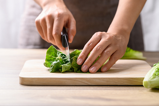 A high angle photo of vegetables on a wooden cutting board with a large knife next to them.  The garlic for the recipe is already in the metal bowl.