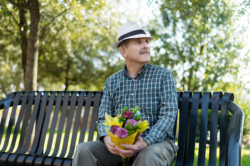 With a heartfelt gesture, the elderly man prepares to surprise his partner with a bouquet of flowers, symbolizing his enduring love and affection.